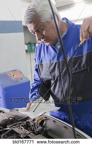 Stock Image - Older Hispanic mechanic repairing car in garage. Fotosearch