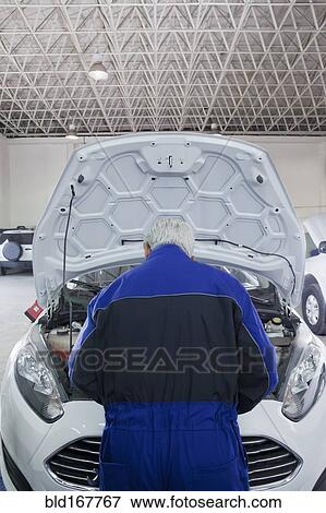 Stock Photo - Older Hispanic mechanic repairing car in garage. Fotosearch