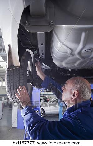 Stock Photo - Older Hispanic mechanic repairing car wheel in garage. Fotosearch