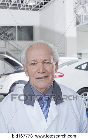 Stock Image - Older Hispanic mechanic standing in garage. Fotosearch
