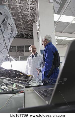 Stock Photo - Older Hispanic mechanics discussing car in garage. Fotosearch