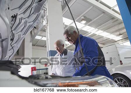 Stock Photo - Older Hispanic mechanics repairing car in garage. Fotosearch