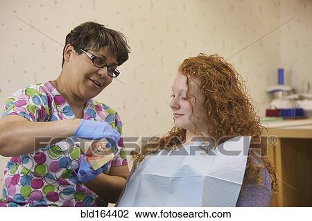 Stock Image - Pediatric dentist showing teeth model to teenage patient. Fotosearch