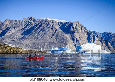 Stock Photograph - People paddling canoe near rock formations in remote river. Fotosearch