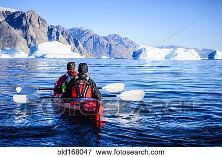 Stock Photo - People paddling canoe towards glaciers in remote river. Fotosearch