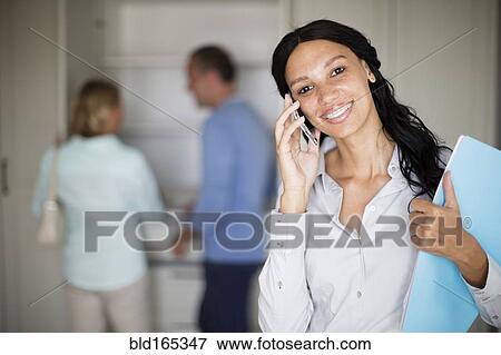 Stock Photo - Realtor talking on cell phone with couple in new home. Fotosearch