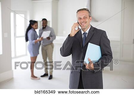 Stock Photo - Realtor talking on cell phone with couple in new home. Fotosearch