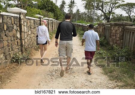 Stock Image - Rear view of friends walking on dirt path. Fotosearch