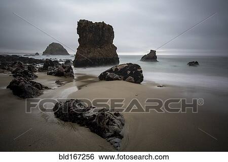 Stock Photograph - Rock formations and ocean waves on sandy beach. Fotosearch