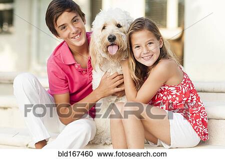Stock Image - Smiling Caucasian brother and sister petting dog outdoors. Fotosearch