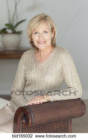 Stock Image - Smiling Caucasian woman sitting on bench. Fotosearch