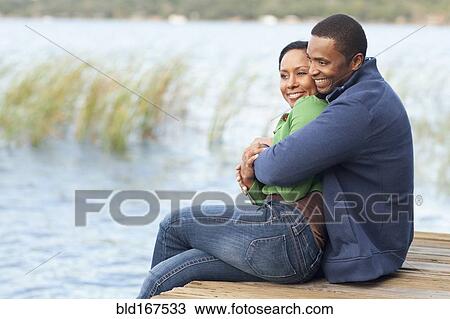 Stock Image - Smiling couple hugging on dock. Fotosearch