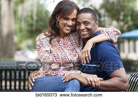 Stock Image - Smiling couple hugging on park bench. Fotosearch