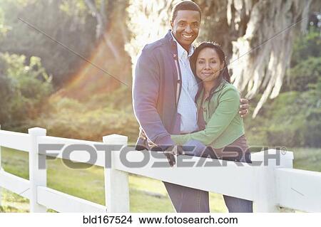 Picture - Smiling couple leaning on fence. Fotosearch