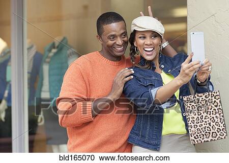 Stock Image - Smiling couple taking selfie outside store. Fotosearch