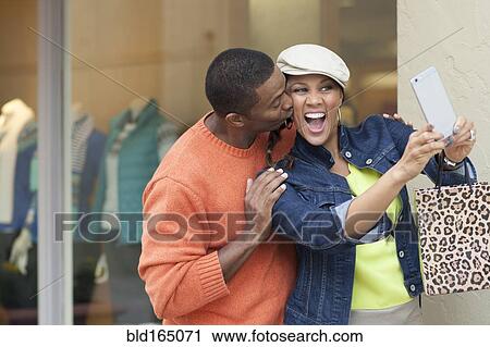 Stock Image - Smiling couple taking selfie outside store. Fotosearch
