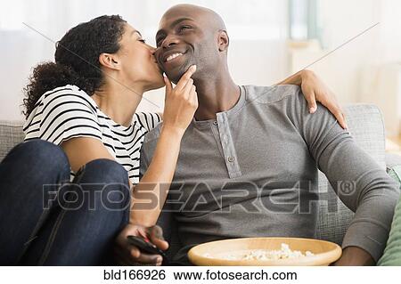 Stock Photograph - Smiling couple watching television on sofa. Fotosearch