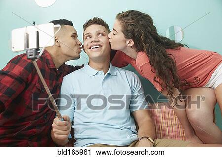 Smiling friends taking selfie kissing cheeks of man View Large Photo Image Stock Image - Smiling friends taking selfie kissing cheeks of man. Fotosearch
