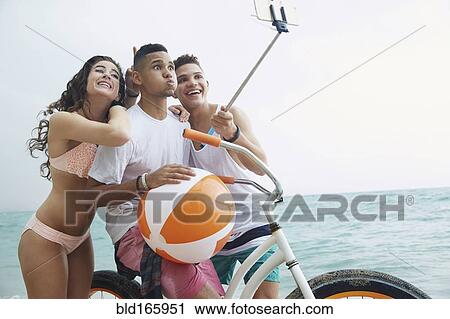 Stock Image - Smiling friends taking selfie on beach. Fotosearch