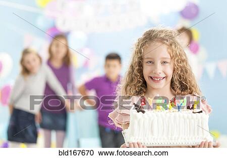 Stock Image - Smiling girl holding birthday cake at party. Fotosearch