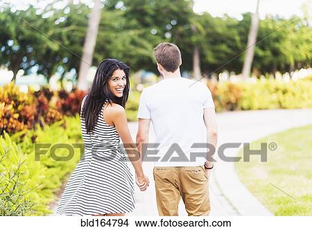 Picture - Smiling Hispanic couple walking in park. Fotosearch