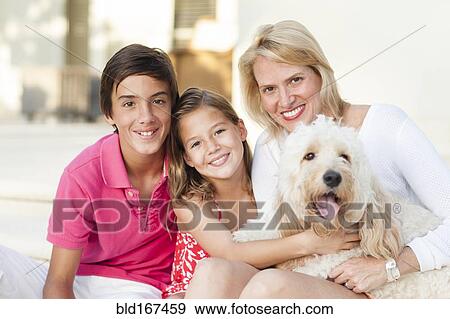 Stock Photo - Smiling mother and children posing with dog outdoors. Fotosearch