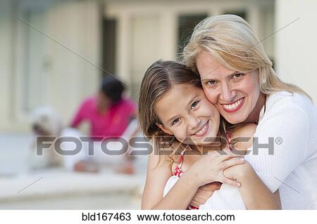 Stock Image - Smiling mother and daughter hugging outdoors. Fotosearch