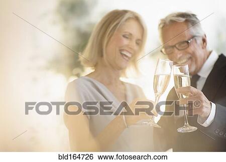 Stock Photograph - Smiling older Caucasian couple toasting with champagne. Fotosearch