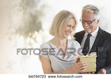 Stock Image - Smiling older Caucasian man giving wife a gift. Fotosearch