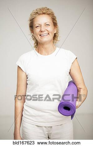 Stock Image - Smiling woman holding exercise mat. Fotosearch