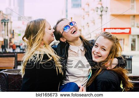 Stock Image - Smiling women hugging in city. Fotosearch