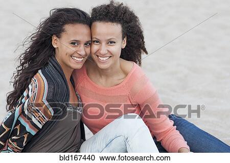 Stock Image - Smiling women hugging on beach. Fotosearch