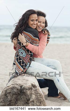 Stock Image - Smiling women hugging on beach. Fotosearch