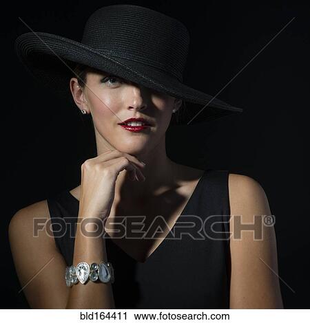 Stock Image - Stylish Caucasian woman wearing black hat and dress. Fotosearch