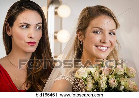 Stock Image - Suspicious bridesmaid standing behind smiling bride. Fotosearch