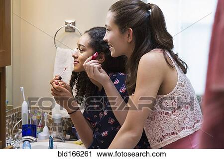 Stock Image - Teenage girls applying makeup in bathroom mirror. Fotosearch