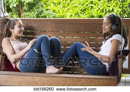 Stock Image - Teenage girls listening to music on porch swing. Fotosearch