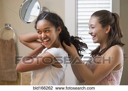 Stock Image - Teenage girls styling hair in bathroom mirror. Fotosearch