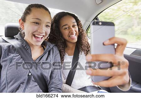 Picture - Teenage girls using cell phone in car back seat. Fotosearch