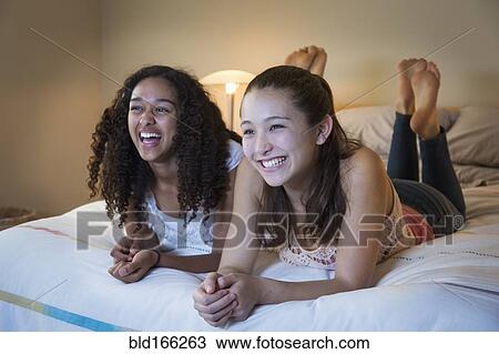 Stock Image - Teenage girls watching television on bed. Fotosearch