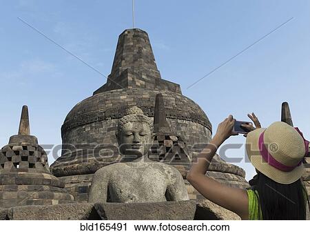 Stock Image - Tourist photographing Buddha statue on Temple of Borobudur, Borobudur, Indonesia. Fotosearch