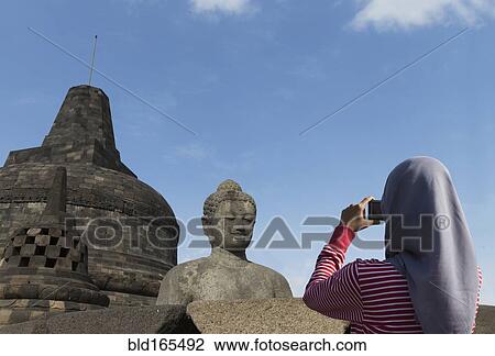 Stock Image - Tourist photographing Buddha statue on Temple of Borobudur, Borobudur, Indonesia. Fotosearch