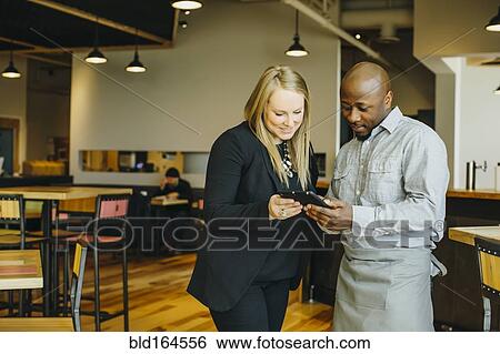 Waiter and businesswoman using cell phones in cafe View Large Photo Image Stock Photograph - Waiter and businesswoman using cell phones in cafe. Fotosearch