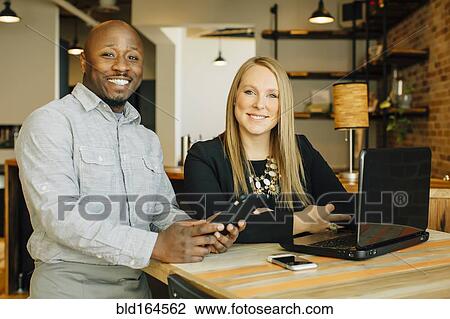 Stock Image - Waiter and businesswoman using technology in cafe. Fotosearch