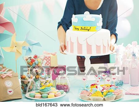 Stock Image - Woman holding birthday cake at party. Fotosearch