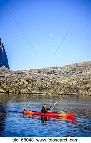 Stock Photo - Woman paddling canoe near rock formations in remote river. Fotosearch