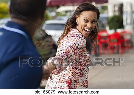 Stock Photo - Woman pulling boyfriend on sidewalk. Fotosearch