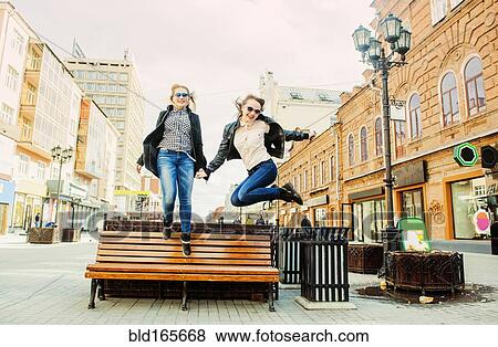 Stock Photo - Women jumping for joy near bench. Fotosearch