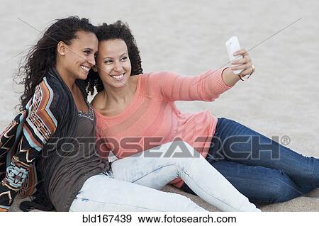 Stock Photo - Women taking selfies on beach. Fotosearch