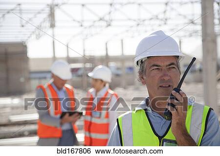 Stock Photograph - Worker talking on walkie-talkie at construction site. Fotosearch